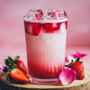 A romantic Valentine’s Day mocktail in a tall glass garnished with fresh strawberries and heart-shaped ice cubes.