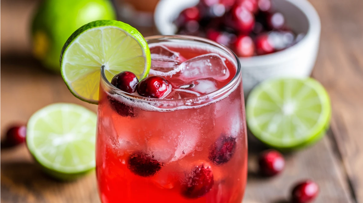 Refreshing Cranberry Mocktail in a tall glass, garnished with lime and mint, surrounded by fresh cranberries and lime wedges.