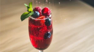 An elegant red mocktail in a champagne flute with floating fresh berries, mint leaves, and rising carbonation bubbles