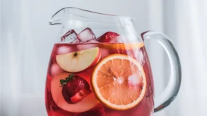 A pitcher of ruby-red non-alcoholic sangria filled with colorful fruit slices and ice cubes