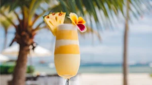 A Tropical Sunrise Mimosa in a champagne flute, layered with orange juice and coconut water. The drink is garnished with a pineapple wedge and tropical flower, evoking a sunny, beachy vibe.