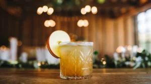 Warm-toned apple ginger mocktail in a glass, garnished with thin apple slice, golden and amber colors, cozy wedding mocktail atmosphere