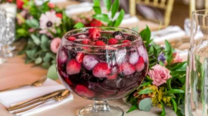 A colorful berry punch with mixed berries floating on top, served in a clear glass punch bowl with a vibrant red and purple hue